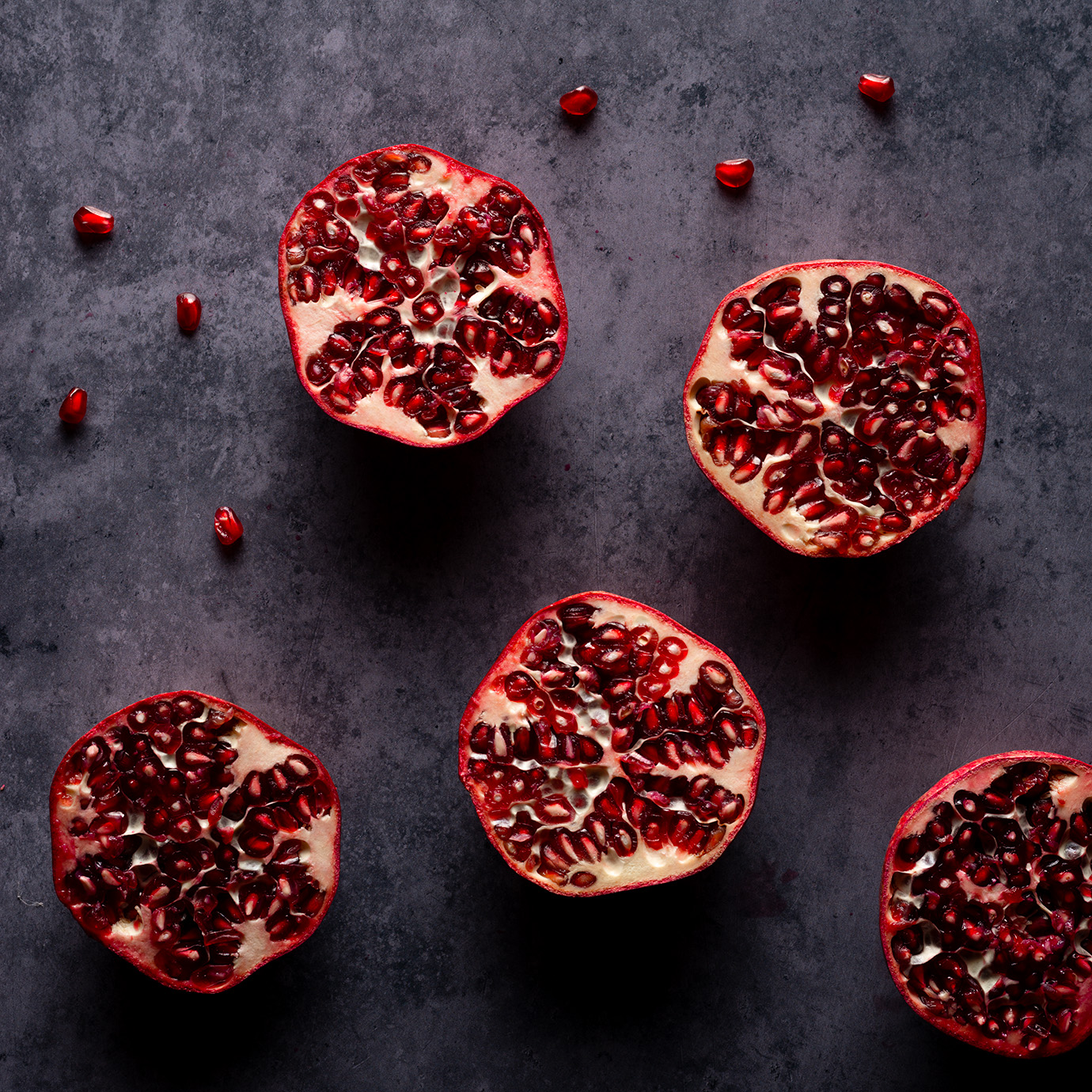 Five pomegranates from above with moody lighting on dark background