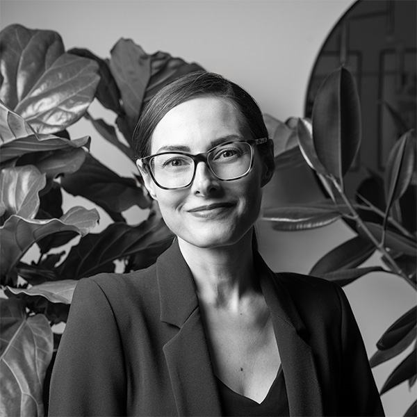 Black and white profile of Mel Discepola in front of large leafy plants, moody lighting